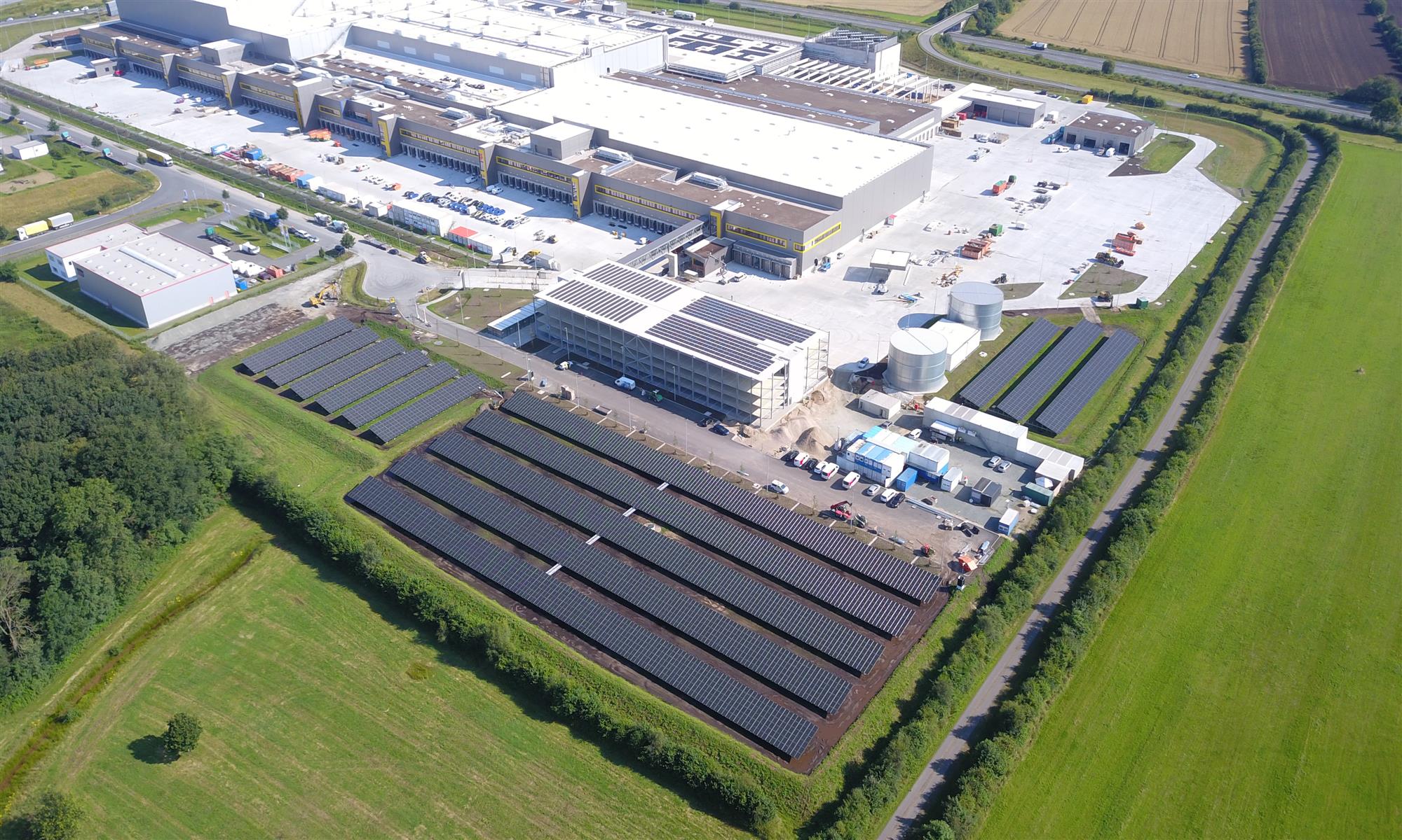 Drohnenaufnahme des Solarparks Neumünster mit Photovoltaik-Modulreihen neben einem Industriekomplex
